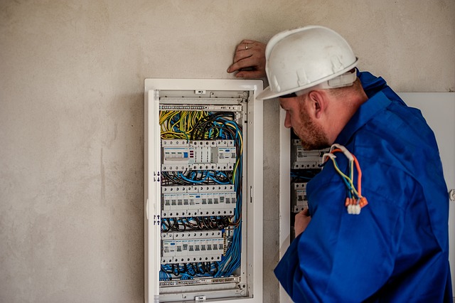 Electrician in a hard hat inspecting the wiring inside an electrical panel